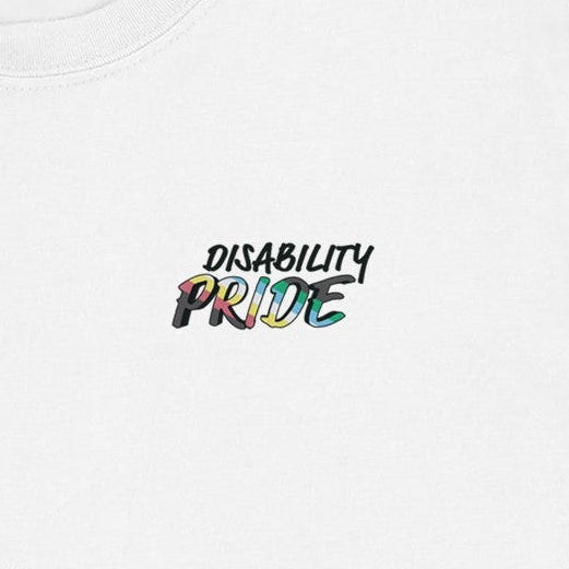 Close-up detail of the words Disability Pride on the chest of a white t-shirt. The word Pride is filled in with colours of the disability pride flag.